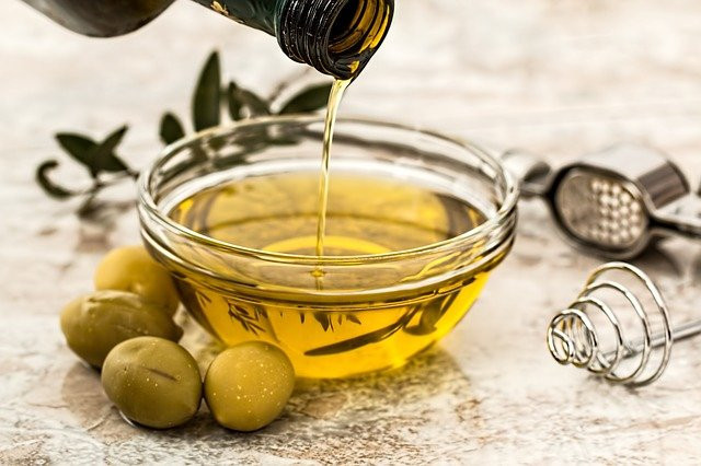 A small bowl of olive oil with a glass bottle of oil being poured into it and whole olives next to it. 
