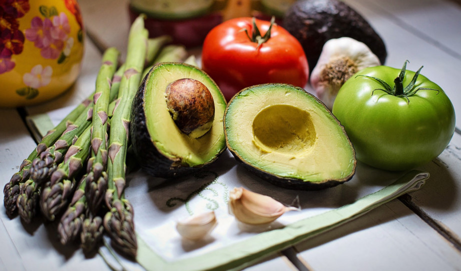 Fresh asparagus, avocado, tomatoes, and garlic cloves on a wooden surface. 