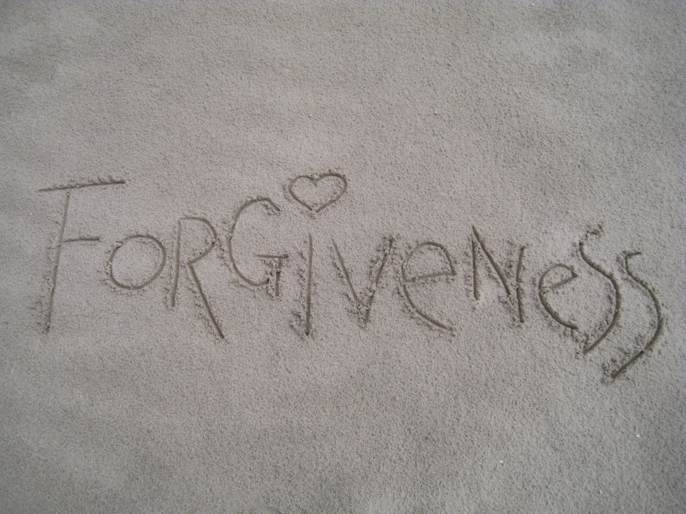 The word forgiveness written in the sand. 