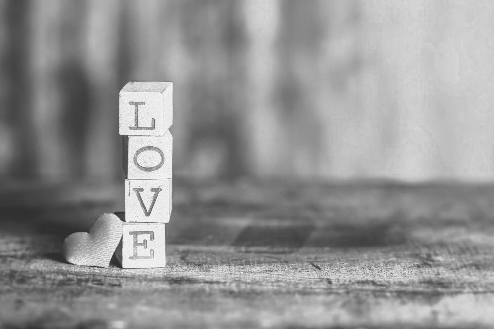 Small blocks with the letters on each that spell out the word love stacked on top of one another with a small heart resting next to it. 