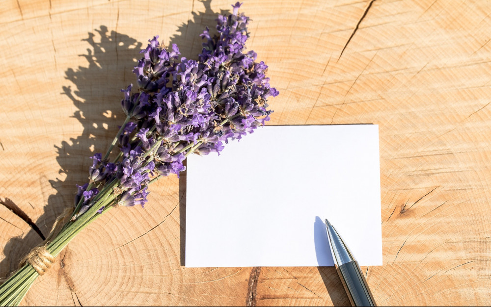 A small piece of paper with a pen resting next to it and a bundle of purple lavender flowers on a wooden background.