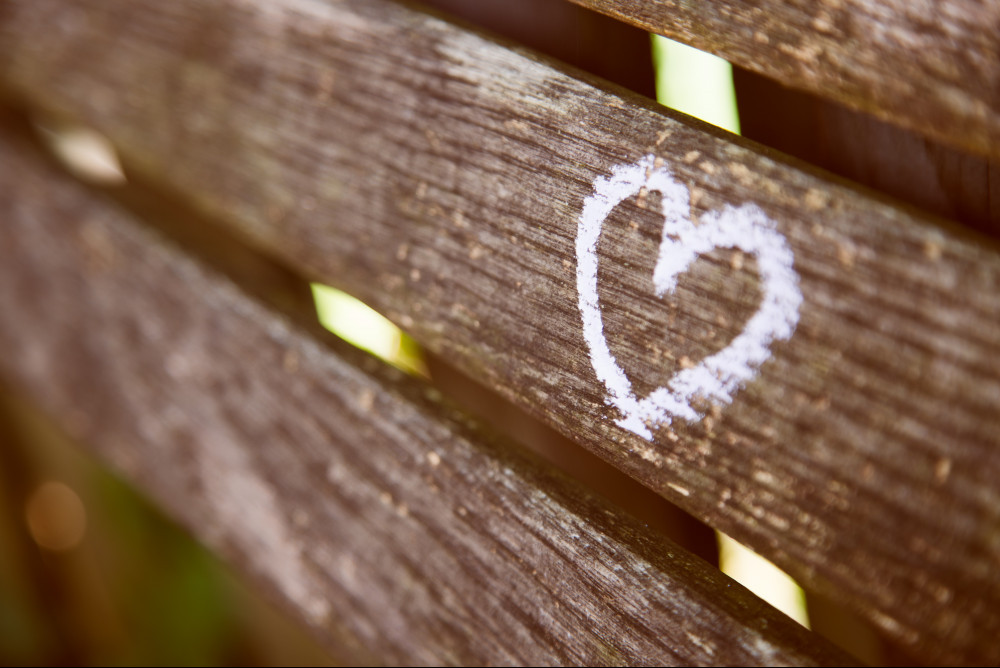 A pink heart written in chalk on the backrest of a wooden bench.