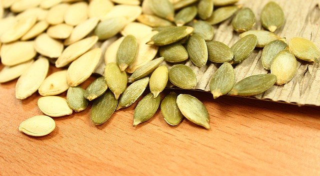 Yellow and green oval shaped pumpkin seeds on a wooden surface.