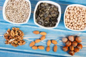 Bowls of nuts and seeds with almonds spelling out the letters Z and N to make the zinc symbol on a blue wooden surface.