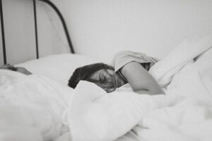 A black & white photo of a woman sleeping in a bed with white bedding.