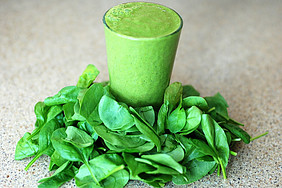A glass of vibrant green juice surrounded by fresh spinach leaves.