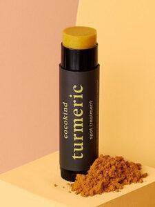 An orange stick of turmeric spot treatment with orange turmeric spice next to it.
