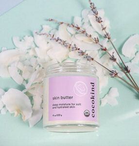 A jar of cocokind skin butter with a purple label with flower petals surrounding it.