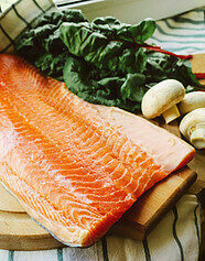 A fresh salmon filet, whole mushrooms, and fresh greens on a cutting board.