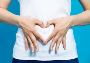 A person making the shape of a heart with their hands over their gut area.