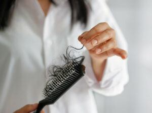 A woman holding a hair brush with a lot of hair in it.