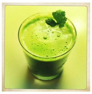 A glass of vibrant green juice with a cilantro garnish. 