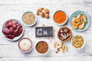 An array of high copper foods such as nuts and seafood surrounding a chalkboard with the copper symbol C-U on it. 
