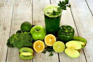 Glass of green juice surrounded by green and yellow fruits and vegetables.