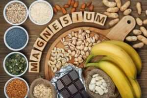 An array of magnesium rich foods such as chocolate, bananas, nuts, and seeds on a wooden surface with the word magnesium spelled in block letters within them.