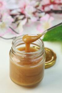 A glass jar of manuka honey with pink manuka tree blossoms in the backround.