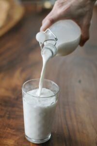 A glass of milk with mik from a glass bottle being poured into it. 