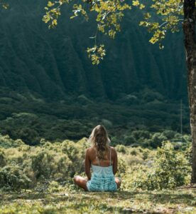 The back view of a woman sitting under a tree in the forest meditating.