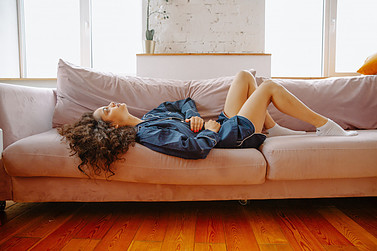 A woman laying on a couch holding her abdomen in pain.