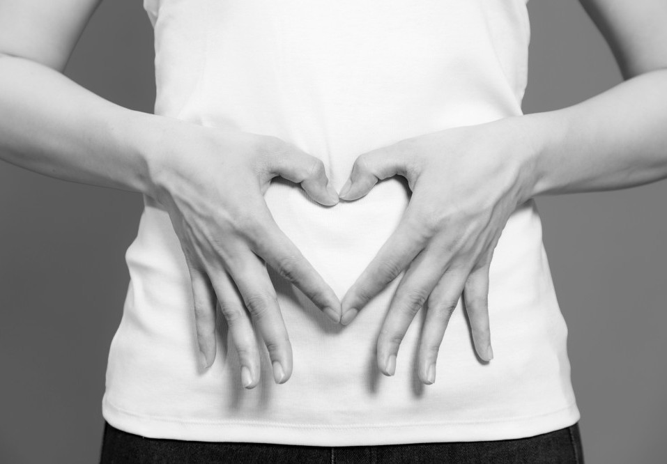 A woman making the shape of a heart with her hands over her gut.