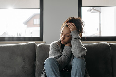 A woman sitting on a couch looking pensive in despair.