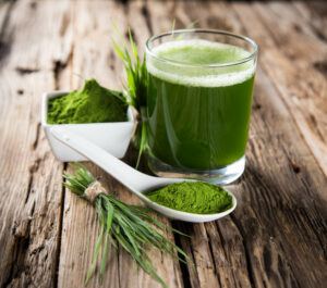 A glass of green juice with green juice powder and wheatgrass.