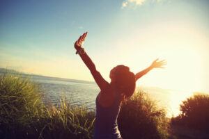 A happy woman with her arms stretched out at sunrise.