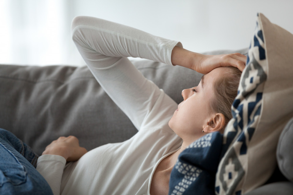 A woman laying on a couch with her hand on her head with illness.