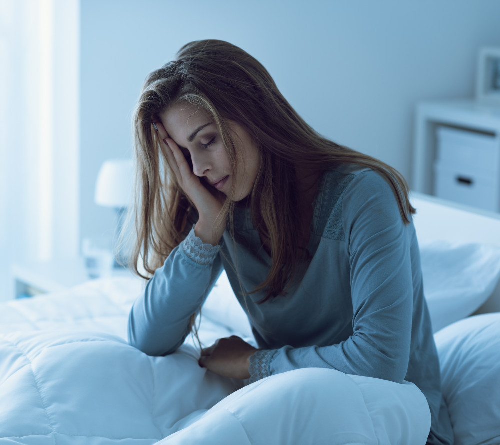 A woman sitting up in bed with her hand on her face feeling ill.