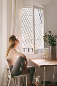 A woman sitting at a table in front of an open window. 