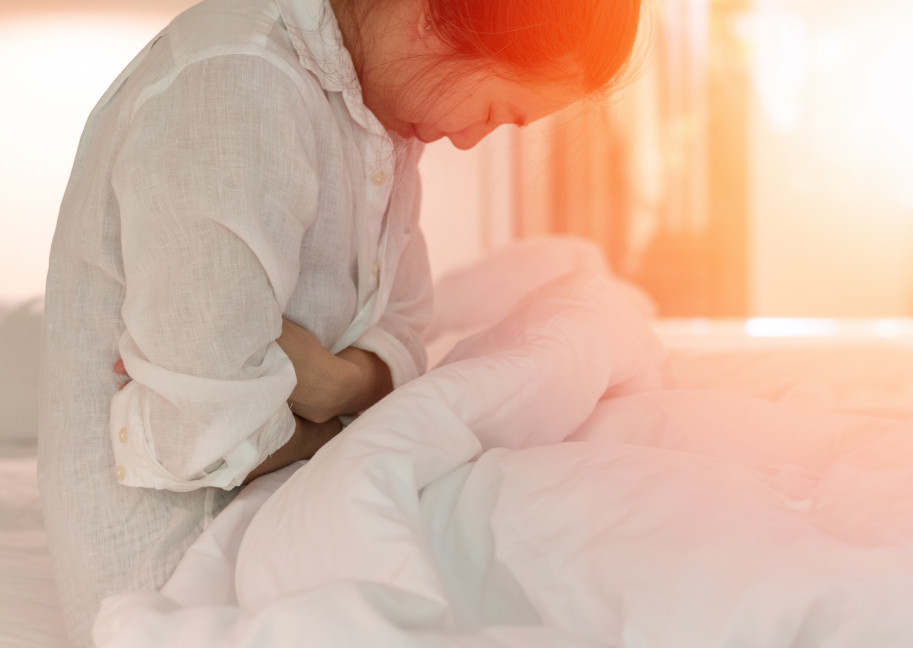 A woman in bed holding her abdomen with endometriosis pain.