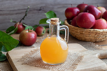 A bottle of raw apple cider vinegar with apples.