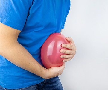A man holding a balloon at his abdomen to represent bloating.